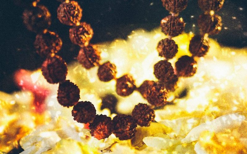 Close-up of a textured brown beaded mala necklace against a golden sparkly blurred background, warm and glowing
